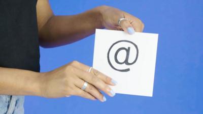 A pair of hands holding a piece of paper with the @ symbol on it