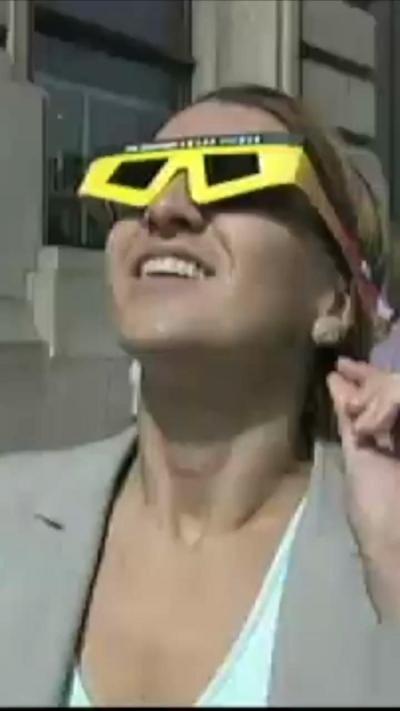 A woman wearing eclipse glasses looks up at the sky