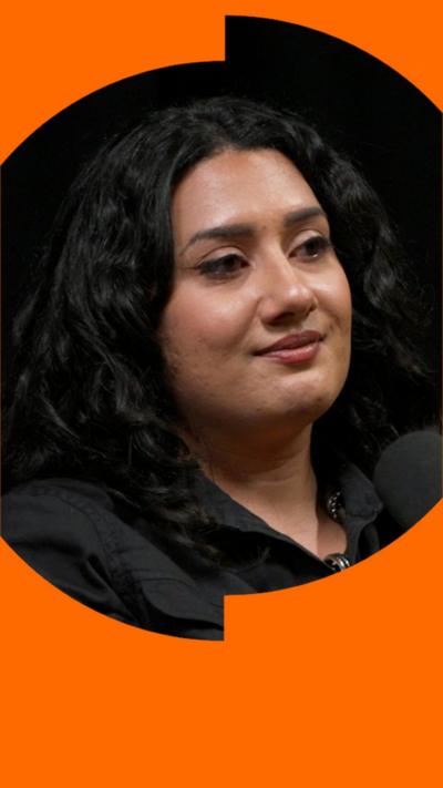A woman with dark, wavy hair smiles at someone off-camera