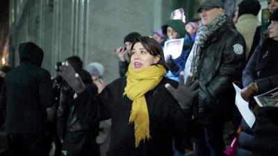 BBC correspondent surrounded by protesters holding photographs