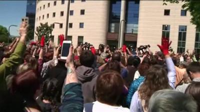 Protesters - some raising a single red-gloved hand - chant in numbers outside the court