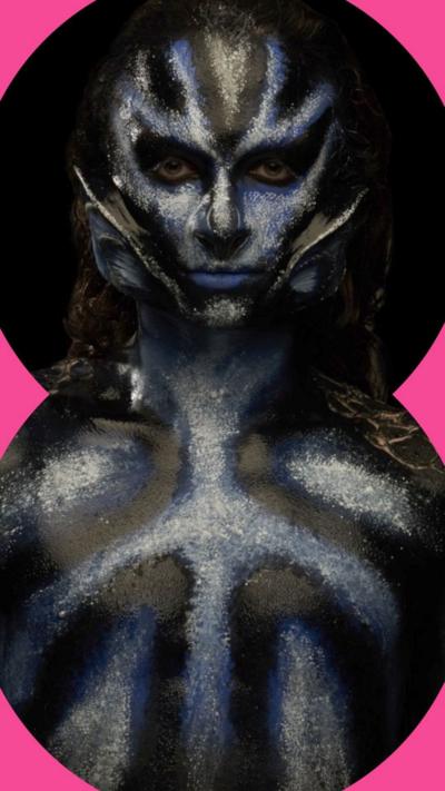 Model with black and blue make-up on their face and body, with prosthetic ears attached to their face