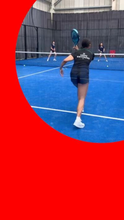A person swings a padel racket. They are wearing shorts and t-shirt and standing on a blue court