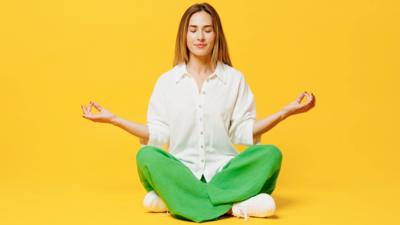 Woman in a white shirt sits cross-legged with her eyes closed 