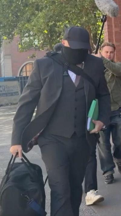 Bush arrives at court. He is wearing a cap and has his face covered