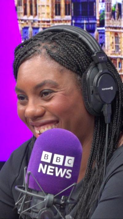 Kemi Badenoch wears headphones and sits in front of a microphone in a radio studio.