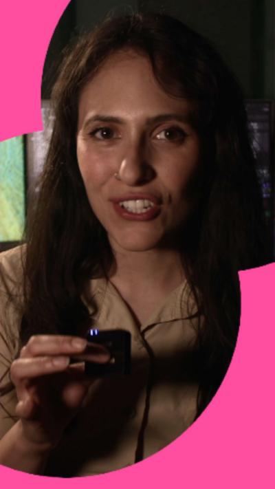  A woman with long dark hair holds a tiny microphone in front of her.