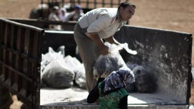 Syrian farmers load bags of dried waste of pressed olives mixed with water in a field near the battled Syrian city of al-Bab