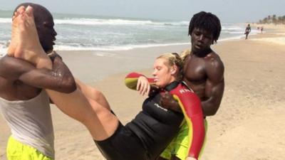 A woman being rescued by two men on beach