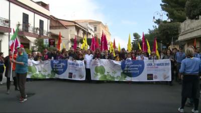 Wide shot of the protest marchers, carrying flags and photographs