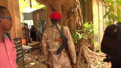 A paramilitary wearing a red beret shouts at some nearby people in this still image