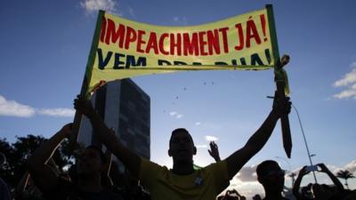 An anti-government protestor holds a sign that reads in Portuguese "Impeachment now!