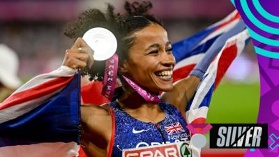 Jazz Sawyers smiles while holding her silver medal by her head, wrapped up in the Union Flag