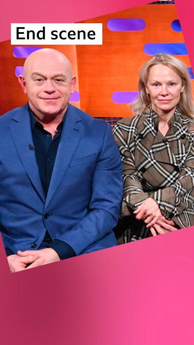 A bald man, Ross Kemp plays air drums while sitting next to Pamela Anderson, who has long blonde hair