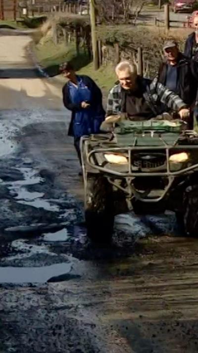 A man in a green four by four off-road vehicle navigating a pothole-ridden lane
