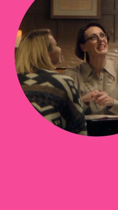 Two women sitting across each other at a table in a restaurant, one is looking up talking to the server off-screen