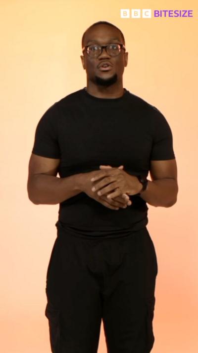 Sage Todz in glasses and a black T-shirt in front of a pale orange background