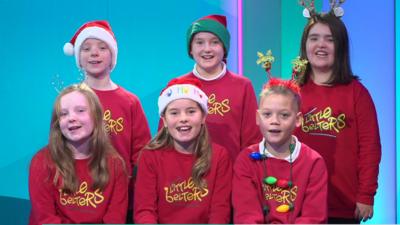 A group of choir children smile at the camera and sing in the Newsround studio.