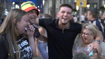 Four Oasis fans cheer in the street.