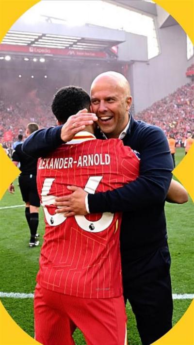 Two men, one in a suit and one in a Liverpool football kit, hug each other. They are standing on  a football pitch in a stadium
