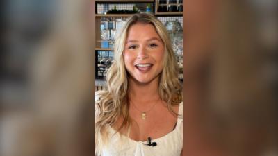 Mollie Pearce smiles in a bar. She has long wavy blonde hair and wears a white top