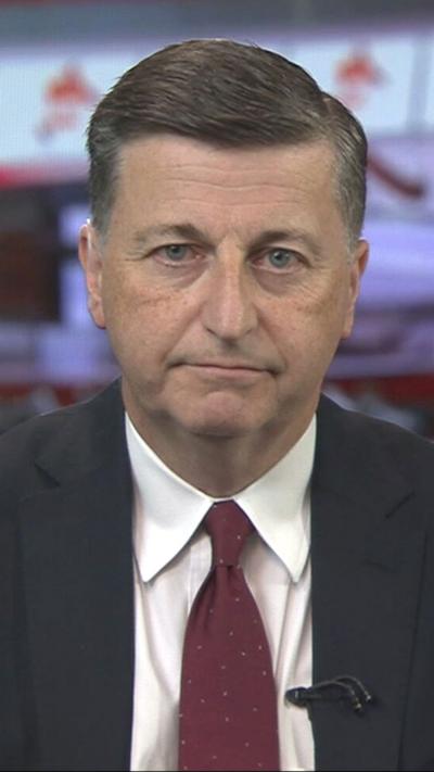 Douglas Alexander sits in a BBC newsroom, he wears a grey suit, cream shirt and burgundy tie