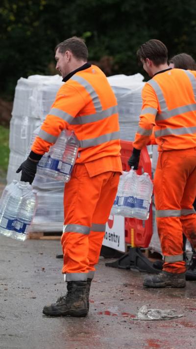 Two men in orange suits lifting bottled water.