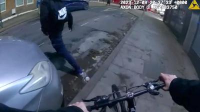 A police officer on a bicycle pursuing a suspect with a black Nike backpack.