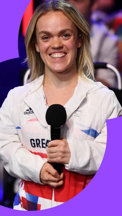 Ellie Simmonds smiles wearing a Great Britain white jacket and holding a mic