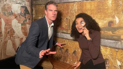 Historian Dan Snow and presenter Nina Blissett strike poses in front of a mock up of an Ancient Egyptian wall engraving.