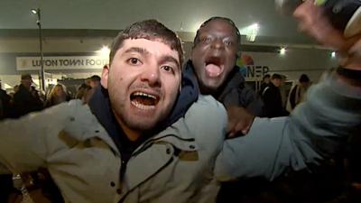 Two happy football fans shouting and cheering at camera.