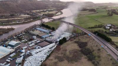 Drone footage of fire are recycling centre next to a river and beside motorway viaduct bridge.