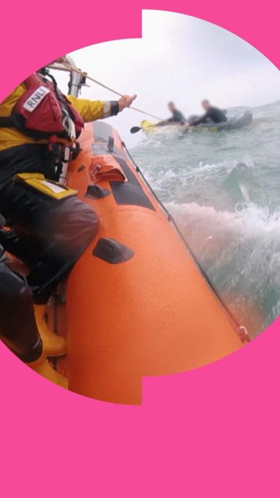 Orange lifeboat with a crew rescuing two people in a kayak in the sea