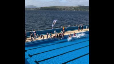 Water splashes as swimmers jump into an outdoor swimming pool