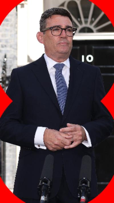 Andy Burnham wearing a suit and a blue tie, standing in front of 10 Downing Street.