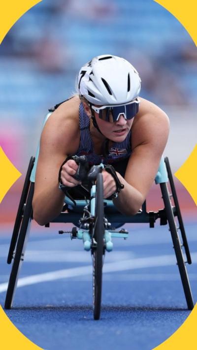 A para athlete racing in a specially adapted wheelchair. She is wearing a white crash helmet, a sun visor and a blue Team GB vest.