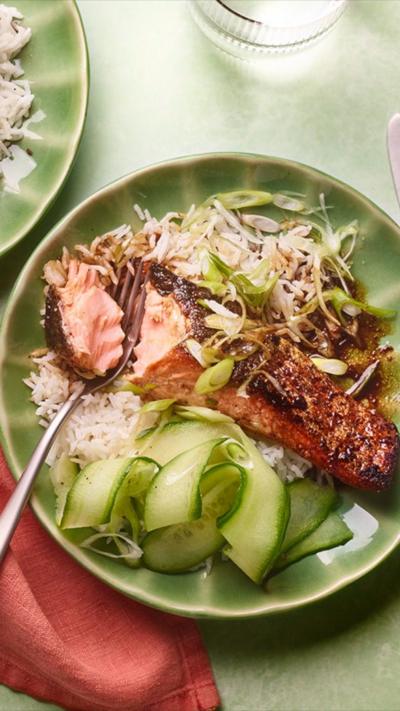 Top down view of a green plates on a green tablecloth with salmon rice and veg on the plate.