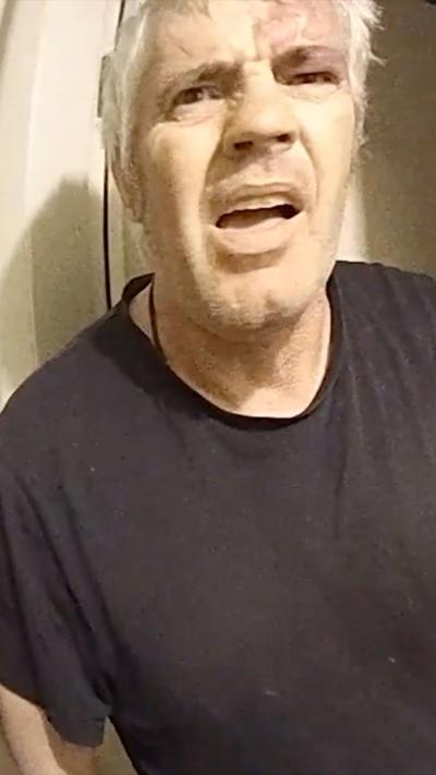 Man in a dark t-shirt with light hair looks angrily at the camera.