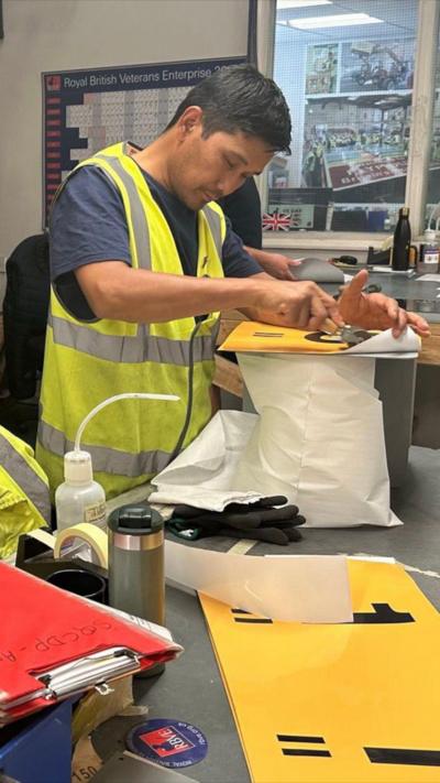 Man in hi vis jacket making a yellow sign at a workbench
