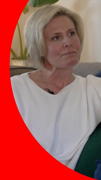 A woman with cropped blonde hair is wearing a long-sleeved white T-shirt. She is sitting on a dark-coloured sofa.