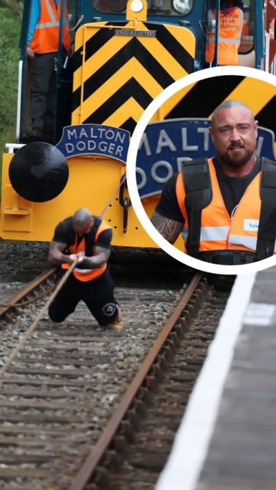 A man in hi vis clothing pulls a train a long a track.
