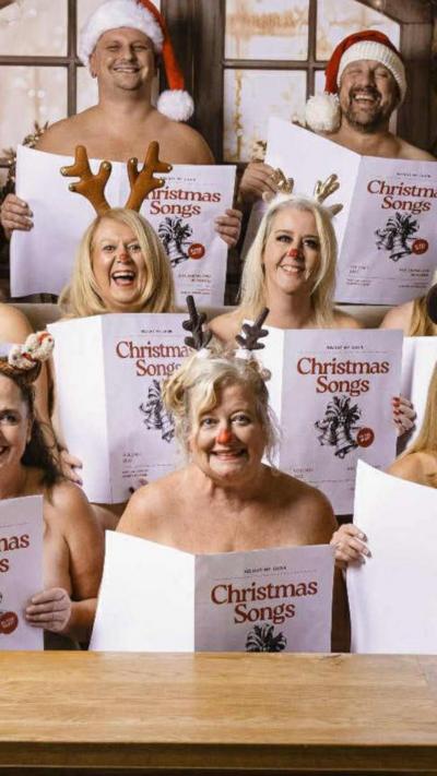 Women wearing reindeer antlers and men in Christmas hats pose in the nude with choir sheets covering them.