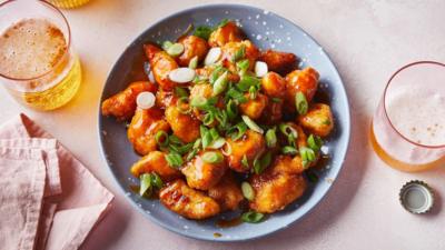 Blue plate with sweet n sour chicken on top. Two glasses of beer at either side.