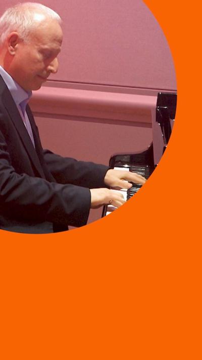 A man, Steve Rosenberg, has short grey hair and wears a suit while he plays the piano