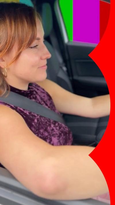 Girl with brown eyes and ginger hair wears gold hoop earrings and a crushed velvet purple vest top and sits in a grey car with her seatbelt fastened.