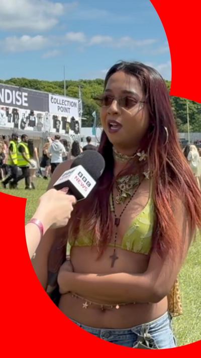 A woman wearing sunglasses and a green bikini top speaks into a BBC News microphone.
