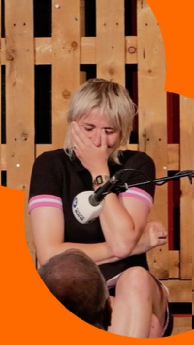 A woman, Maisie Adam, with short blonde hair is laughing with her left hand covering her mouth.