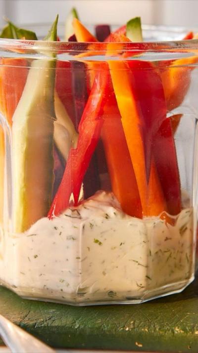 Vegetable sticks on top of a light coloured dip in a glass