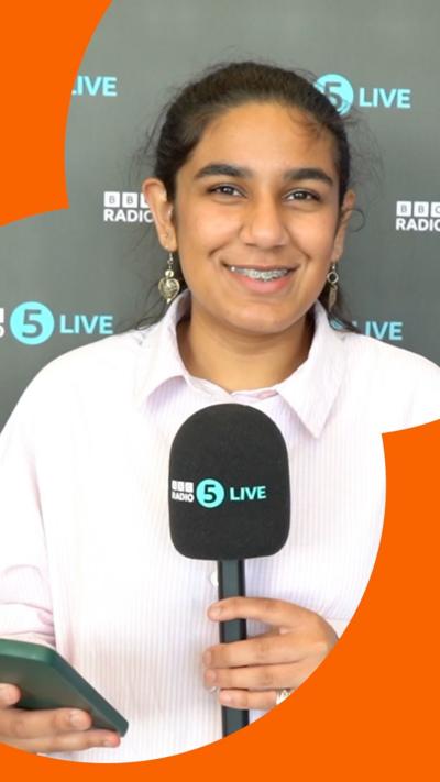 A teen smiles in front of a microphone. She wears a white shirt.