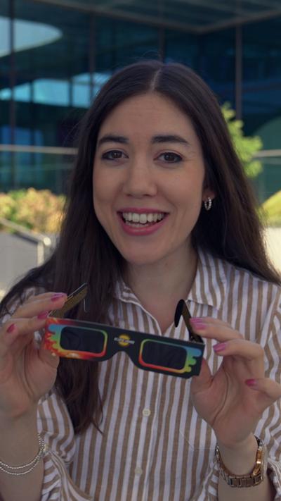 Sabrina Lee, who has long black hair, holding a pair of eclipse glasses, and a striped shirt